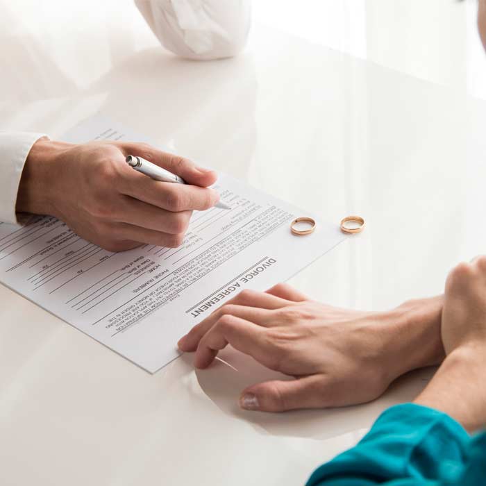 En esta imagen aparece dos personas en una mesa, con dos anillos sobre la mesa y firmando un documento de divorcio. Esta imagen pertenece a la descripción de la sección derecho de Familia.
